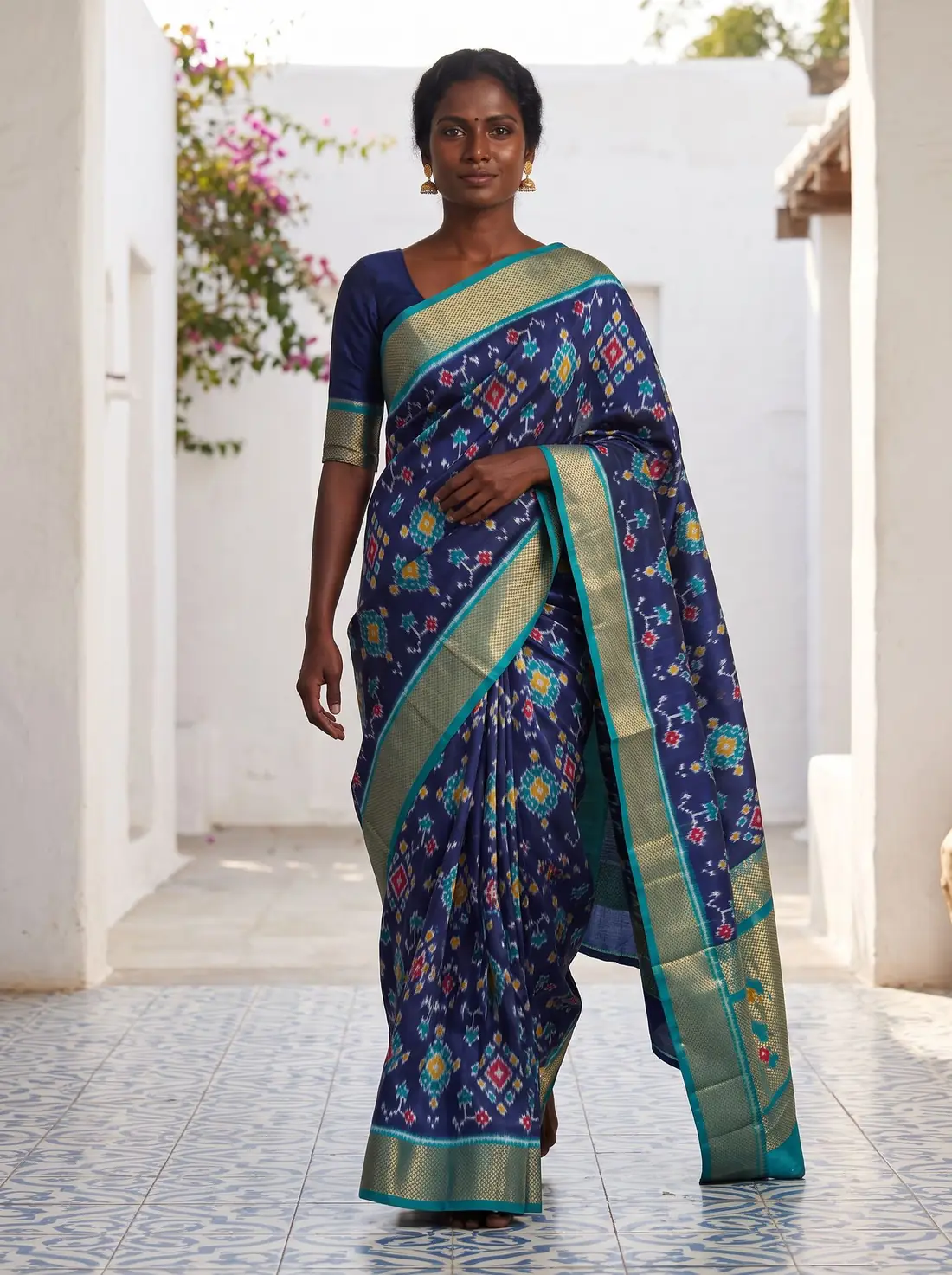 Woman in a navy Pochampally ikat saree walking through a sunlit courtyard
