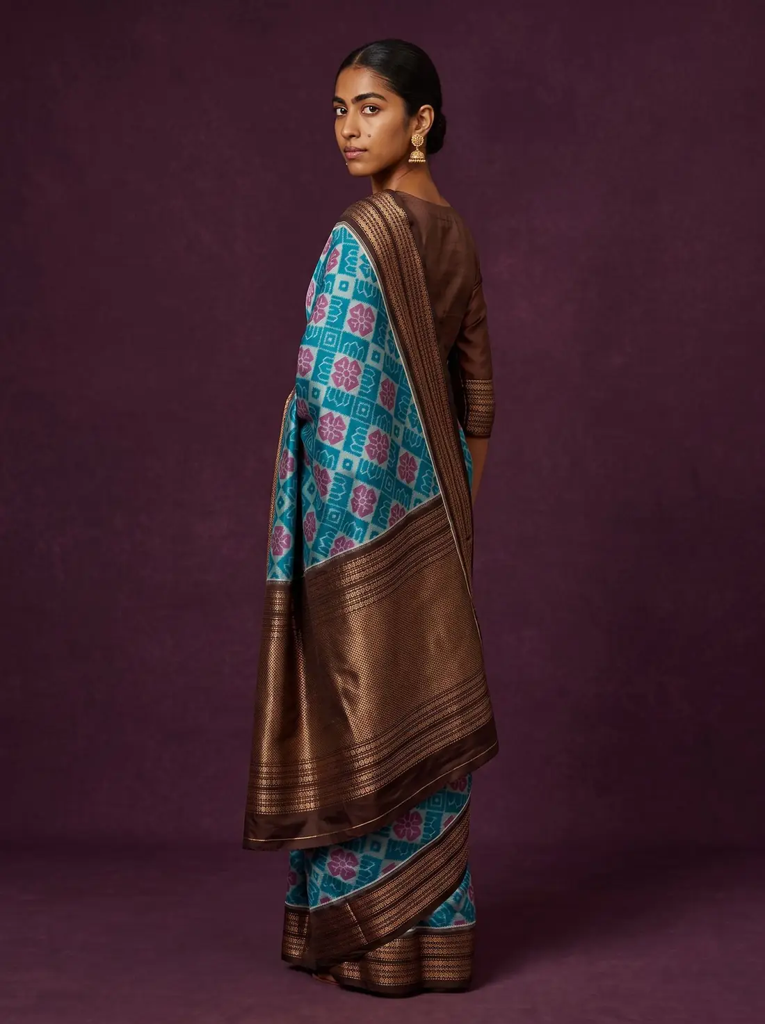 Woman in a turquoise Sambalpuri ikat saree looking over her shoulder